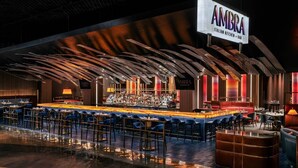 A bar area with a long counter, multiple seating options, and a prominent sign for 'AMBRA Italian Kitchen + Bar'.