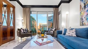 A modern living room with a glass coffee table, blue sofa, and two armchairs.