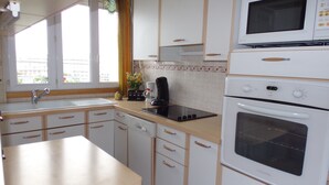 A kitchen with white cabinets, a microwave, an oven, a sink, and a window with curtains. - Sweet Home Panoramic Sacré Coeur  (Paris)