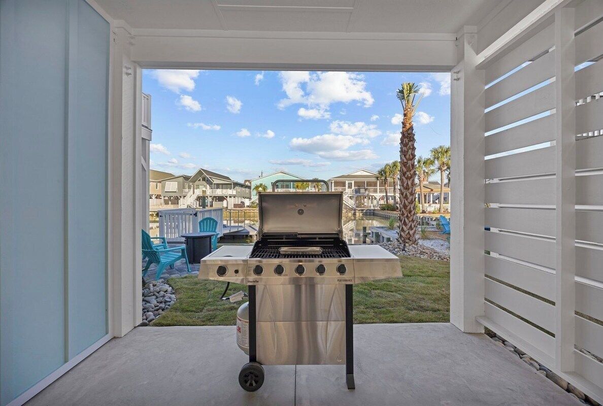 Eine Terrasse mit Grill, Blick auf Häuser und eine Palme.