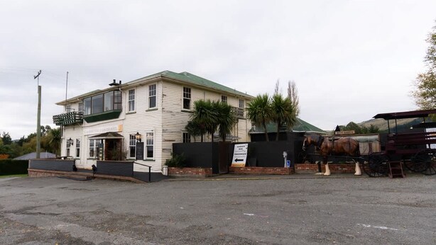 A two-story building with a green roof, a sign indicating a garden, and a horse-drawn carriage. - Weka Pass Cottages 3 by Tiny Away (Waikari)