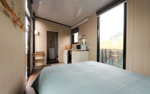 A bedroom with a bed, a desk, a chair, a microwave, and a view through a large window. - Weka Pass Cottages 3 by Tiny Away (Waikari)