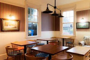 A dining area with wooden tables and chairs, large windows, and wall-mounted light fixtures. - Weka Pass Cottages 3 by Tiny Away (Waikari)