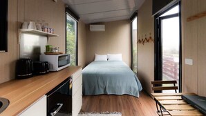 A modern bedroom with a bed, a small kitchenette, and a large window providing a view of the outdoors. - Weka Pass Cottages 3 by Tiny Away (Waikari)
