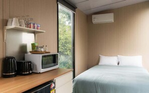 Een hotelkamer met een bed, een magnetron, een koffiezetapparaat en een plank met glazen en snacks.