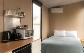 Una habitación de hotel con una cama, microondas, cafetera y repisa con vasos y una botella.