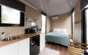 A compact room with a kitchenette, a bed, a window, and a bench. - Weka Pass Cottages 4 by Tiny Away (Waikari)