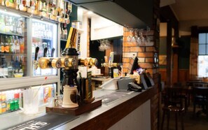 Een bar met een koffieapparaat, een kassa en een koelkast vol drankjes.