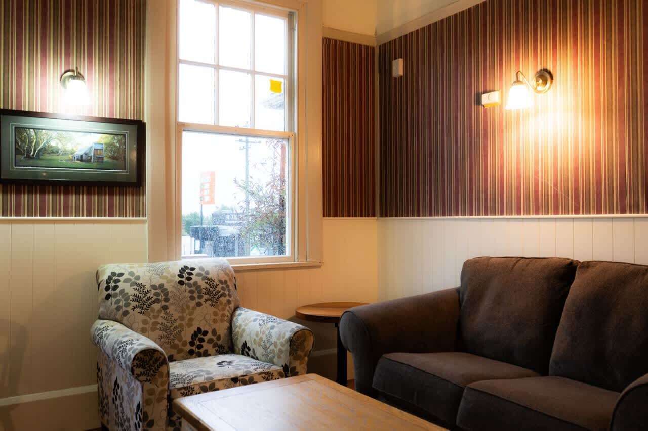 A room with a patterned armchair, a dark sofa, a small table, and a window with a view of trees.