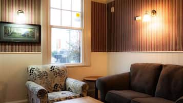 A room with a patterned armchair, a dark sofa, a small table, and a window with a view of trees.