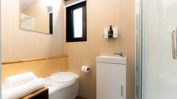 A compact bathroom with a toilet, a small sink, a mirror, and a window.