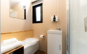 A compact bathroom with a toilet, a small sink, a mirror, and a window. - Weka Pass Cottages 4 by Tiny Away (Waikari)