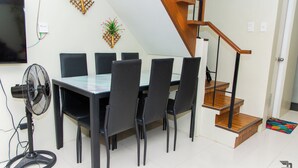 Un'area pranzo con tavolo e sedie, una ventola a piantana, una TV e una scala.