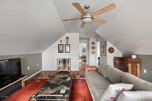 Un ampio soggiorno con ventilatore a soffitto, un'ampia TV a schermo piatto, un divano, un tappeto decorato e un camino.