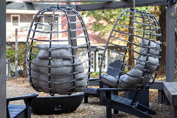 Two hanging chairs with cushioned seats and backs, suspended by a net-like structure, in an outdoor setting with a wooden deck and a building in the background.