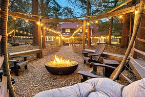An outdoor seating area with a fire pit, wooden benches, and string lights. - Beautiful Villa - Hot Tub, Sauna, Home Theater, GameRoom, EV, 7 Bdrms, Slps 24 (Arden)