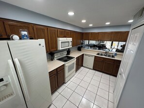 A kitchen with wooden cabinets, a white refrigerator, a microwave, a stove, and a dishwasher. - Ocean View Condo • Pool • Beachy Getaway (Cocoa Beach)