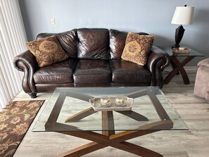 A living room with a leather sofa, a glass coffee table, and a patterned rug. - Ocean View Condo • Pool • Beachy Getaway (Cocoa Beach)