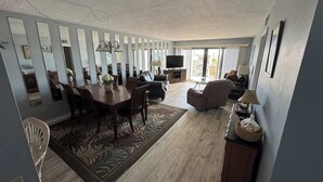 Uma sala de estar espaçosa com área de jantar, TV de tela plana e uma janela grande que traz luz natural.
