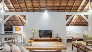 A spacious living area with a wooden ceiling, a central table with a flat-screen TV, a sofa, and a dining table with chairs. - Charming 3-bedroom family villa in Berawa (Bali)