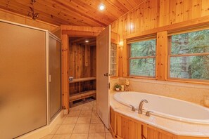 A wooden cabin interior with a large bathtub, a window with a forest view, and a door leading to a hallway. - Summer Lodge Life! 5bd+4bath+HotTub+Sauna+EV (Ashford)