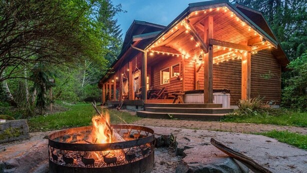A wooden cabin with a fire pit in front, surrounded by trees. - Summer Lodge Life! 5bd+4bath+HotTub+Sauna+EV (Ashford)