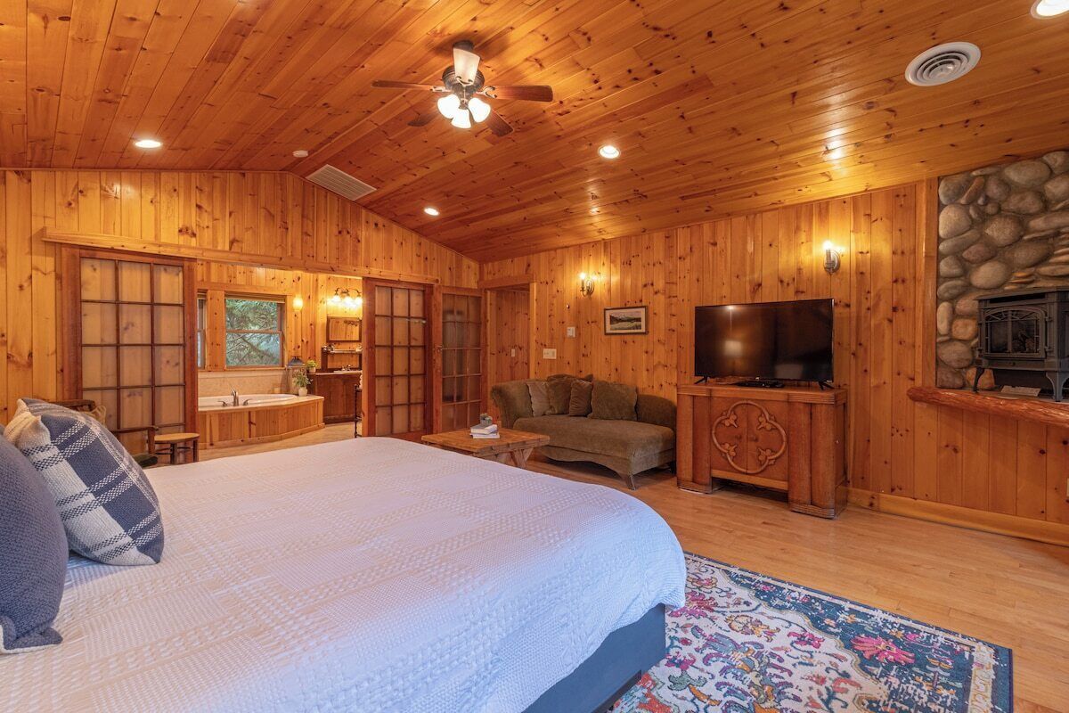 Ein Schlafzimmer in einer Blockhütte mit Bett, Fernseher, Kamin und einer Steinwand.