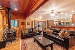 A cozy cabin interior with a fireplace, leather sofas, a coffee table, and a kitchen area. - Summer Lodge Life! 5bd+4bath+HotTub+Sauna+EV (Ashford)