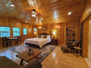 A wooden-paneled room with a bed, a desk, a chair, a bookshelf, and a fireplace. - Summer Lodge Life! 5bd+4bath+HotTub+Sauna+EV (Ashford)