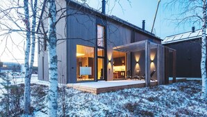 Ein modernes Haus mit großen Glasfenstern, einer Holzdiele und einer verschneiten Landschaft.