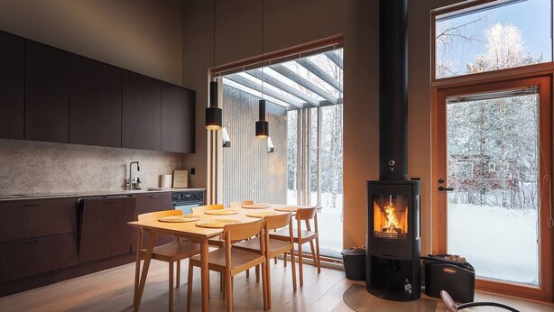 Eine moderne Küche mit dunklen Schränken, einem Holztisch, Pendelleuchten und einem Kaminofen.