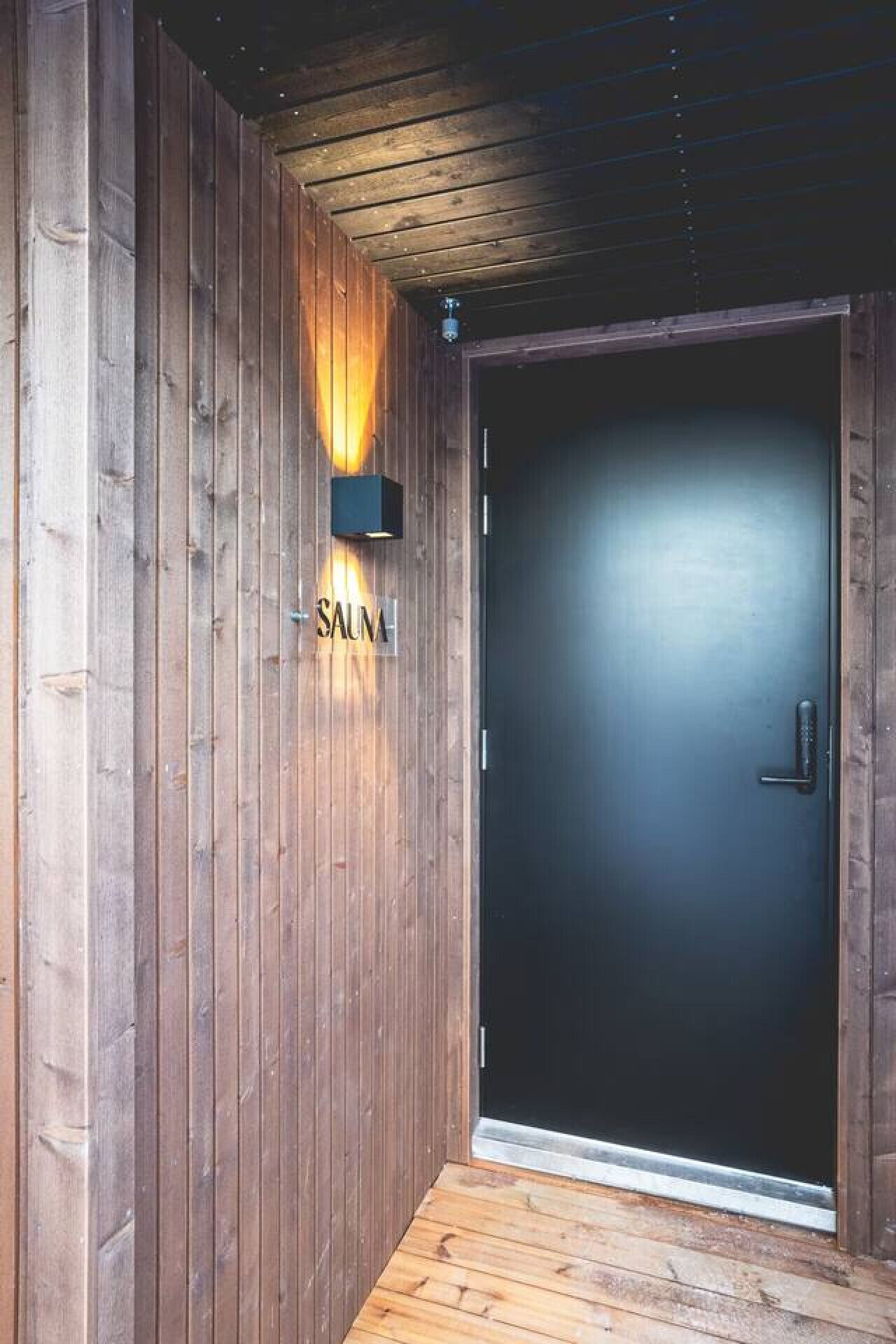 Una porta de fusta amb un rètol que diu "SAUMA" i una petita llum penjant a sobre.