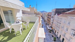 Una terrassa al terrat amb una taula i cadires, vista d'un carrer amb edificis i un cel serè.