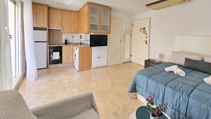 Habitació d'hotel petita amb cuineta, un llit, un sofà i un bany modest.