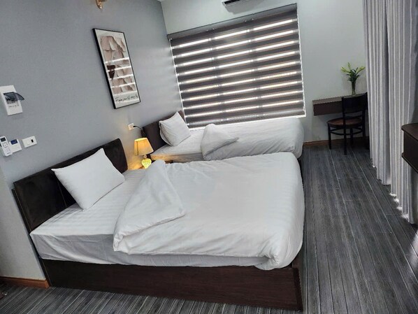A double bed with white bedding, a bedside table with a lamp, a framed picture on the wall, and a window with blinds. - Sunshine Mini Hotel (Van Xuan)