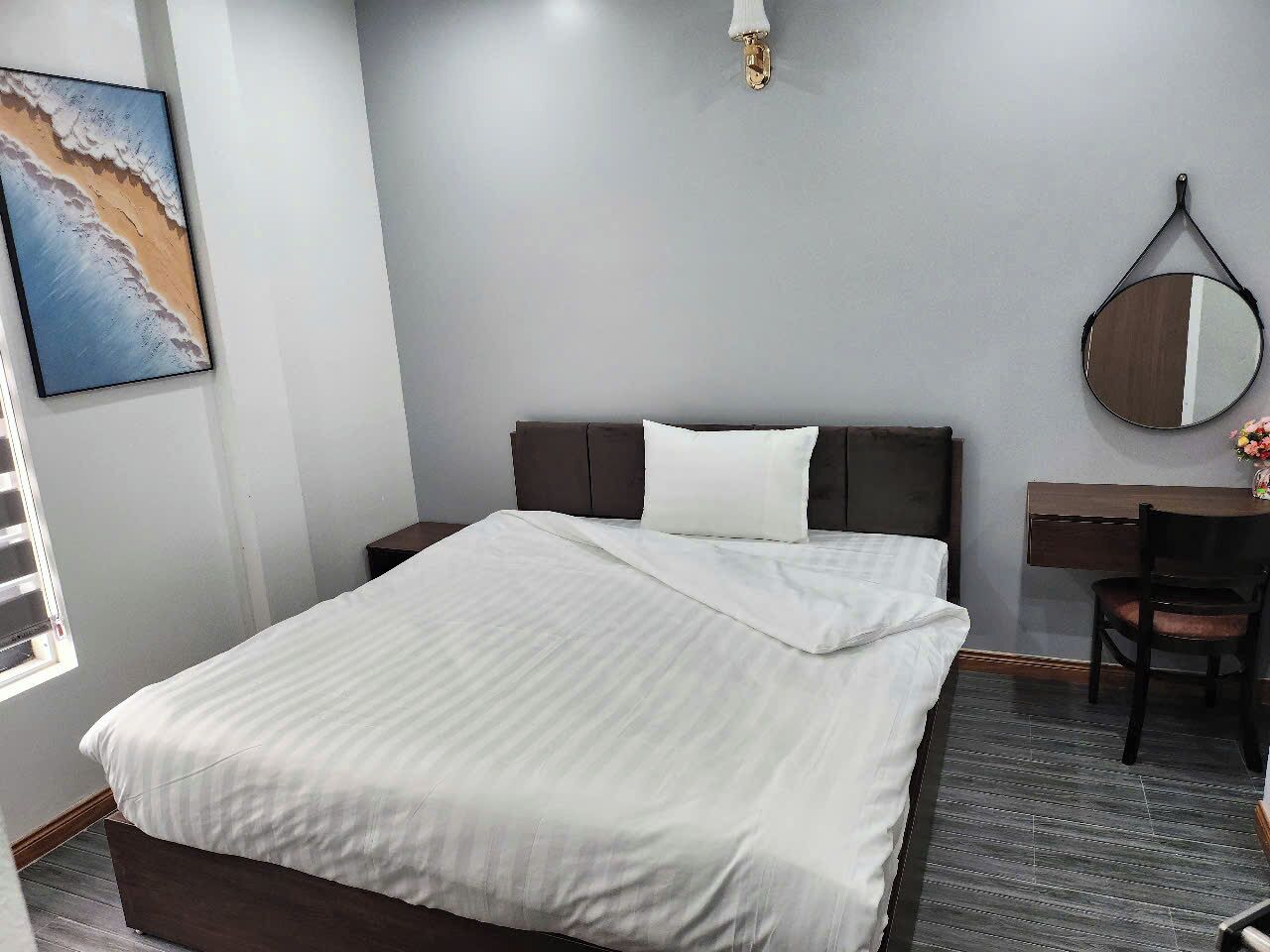 Habitación de hotel con cama, escritorio, silla, espejo y un cuadro en la pared.