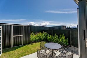 A patio with a round table and chairs, surrounded by a metal fence and greenery.