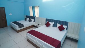Ein Hotelzimmer mit zwei Betten, einem Deckenventilator, einem Fenster mit Vorhängen und einem kleinen Oberlicht.