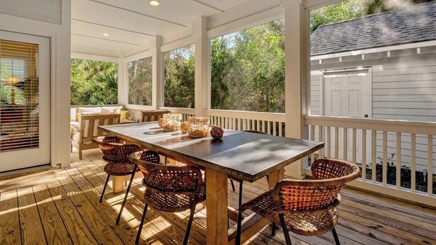 A covered outdoor deck with a table and chairs, a ceiling fan, and a view of the surrounding trees.