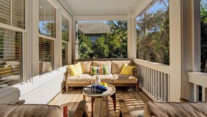 A covered porch with a beige sofa, wooden furniture, and large windows.
