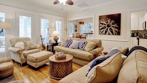 A living room with a sofa, armchair, and ottoman, a ceiling fan, and a large wall clock.