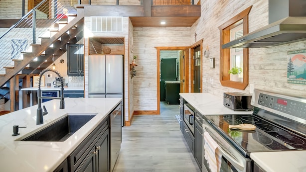 Une cuisine moderne dotée d’un îlot central, d’appareils électroménagers en acier inoxydable et d’un escalier en bois.