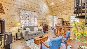 A cozy cabin interior with a sofa, chairs, a dining table, a kitchen area, and a fireplace. - Near Greenbrier River! Mtn-View Cabin w/ Fire Pit (Marlinton)