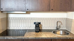 Een keuken met houten kastjes, een roestvrijstalen spoelbak, een zwarte koffiezetapparaat en een achterwand van hexagontegels.