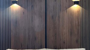 Een bank met twee kussens tegen een houten wand, met daaraan twee wandlampen.