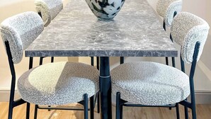 Een eettafel met een bloevas, omringd door stoelen met gestructureerde kussens.