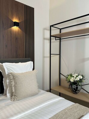 A modern bedroom with a wooden headboard, a bedside table with a vase of flowers, and a black metal shelf unit.