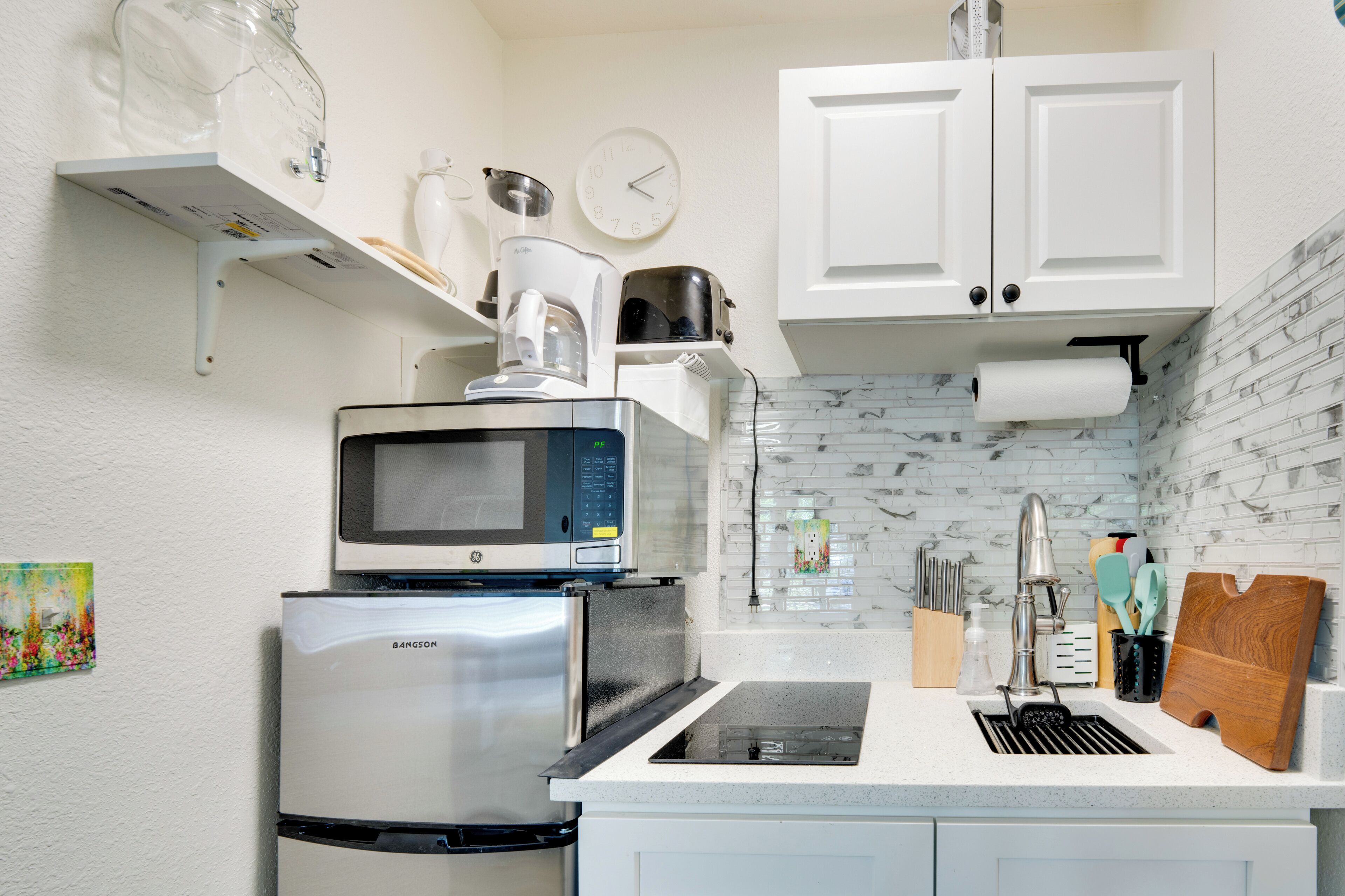 A modern kitchen with a stainless steel refrigerator, microwave, and coffee maker on a white countertop.