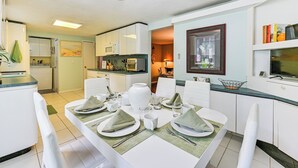 Una cocina moderna con armarios blancos, una mesa de comedor con servilletas y platos verdes, y un ventilador de techo.