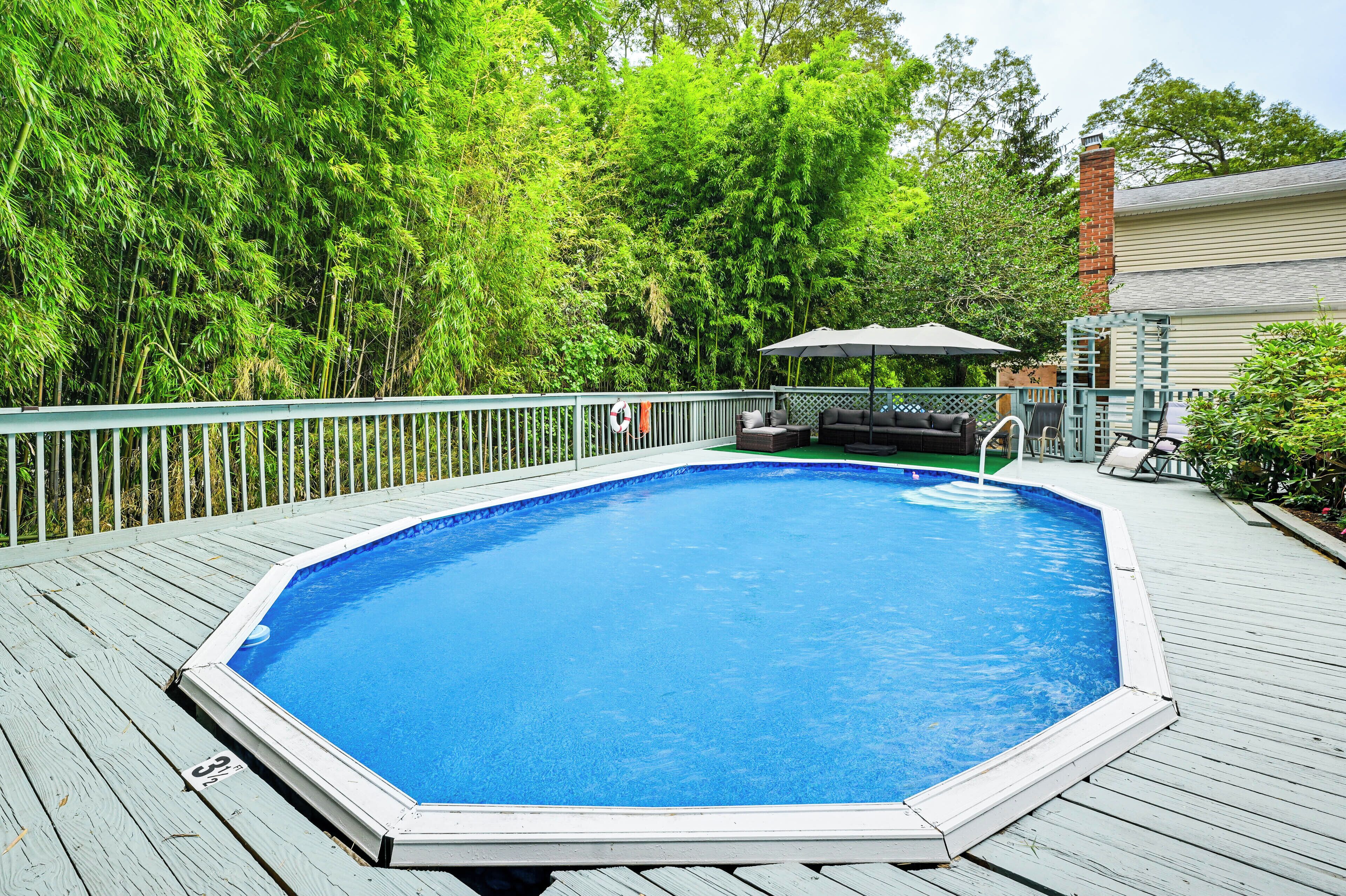 Une piscine extérieure dotée d’une terrasse en bois, entourée d’arbres verdoyants.